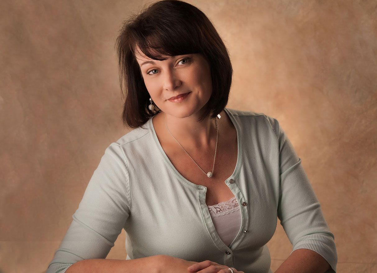 Portrait of our photographer Tracey Luttgens wearing a light blue cardigan and a necklace smiles for the camera, as captured by Master Photographer Tim Kelly of Sanford, Florida.