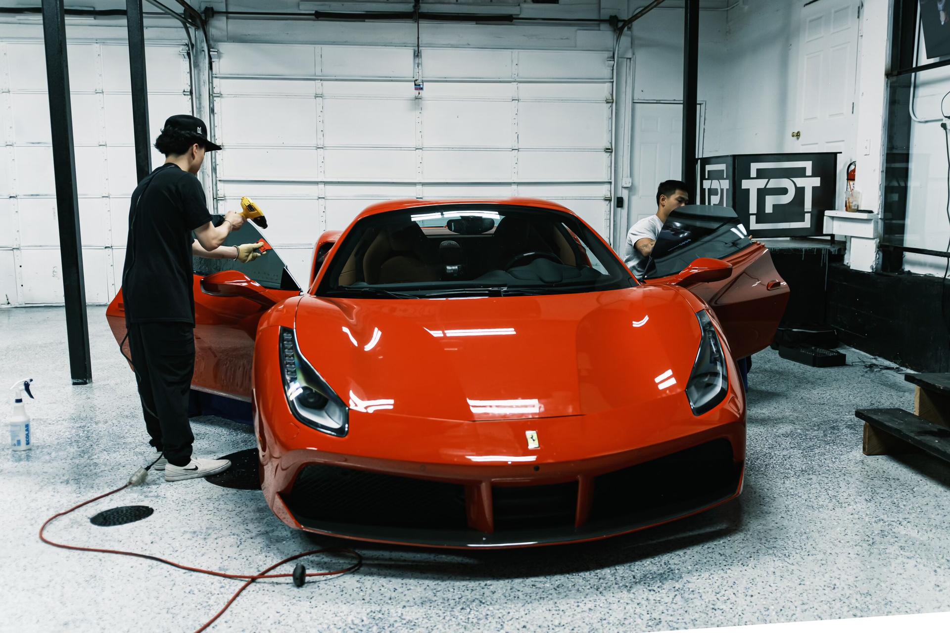 Two men are working on a red sports car in a garage.