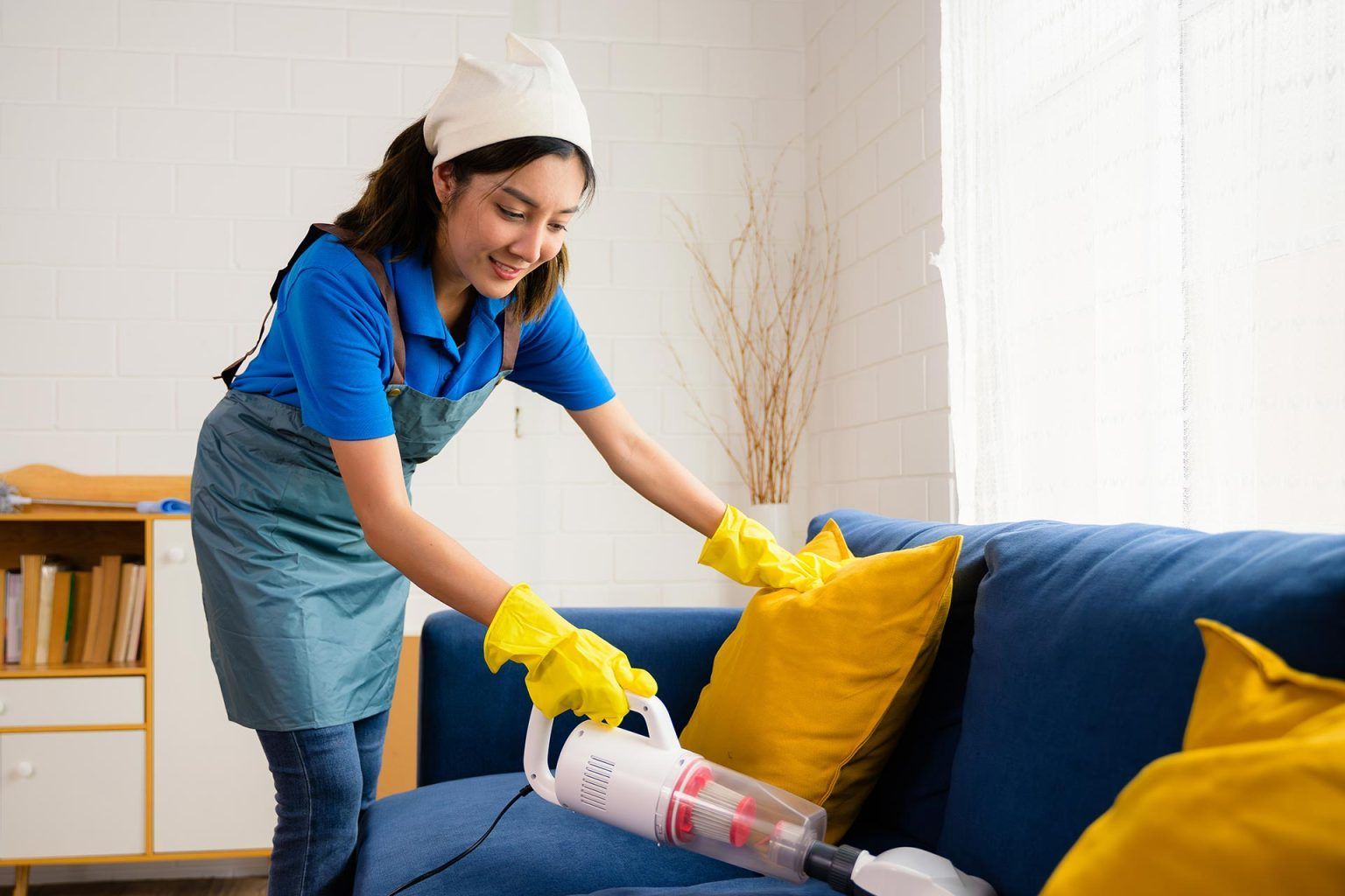 A woman is cleaning a couch with a vacuum cleaner.