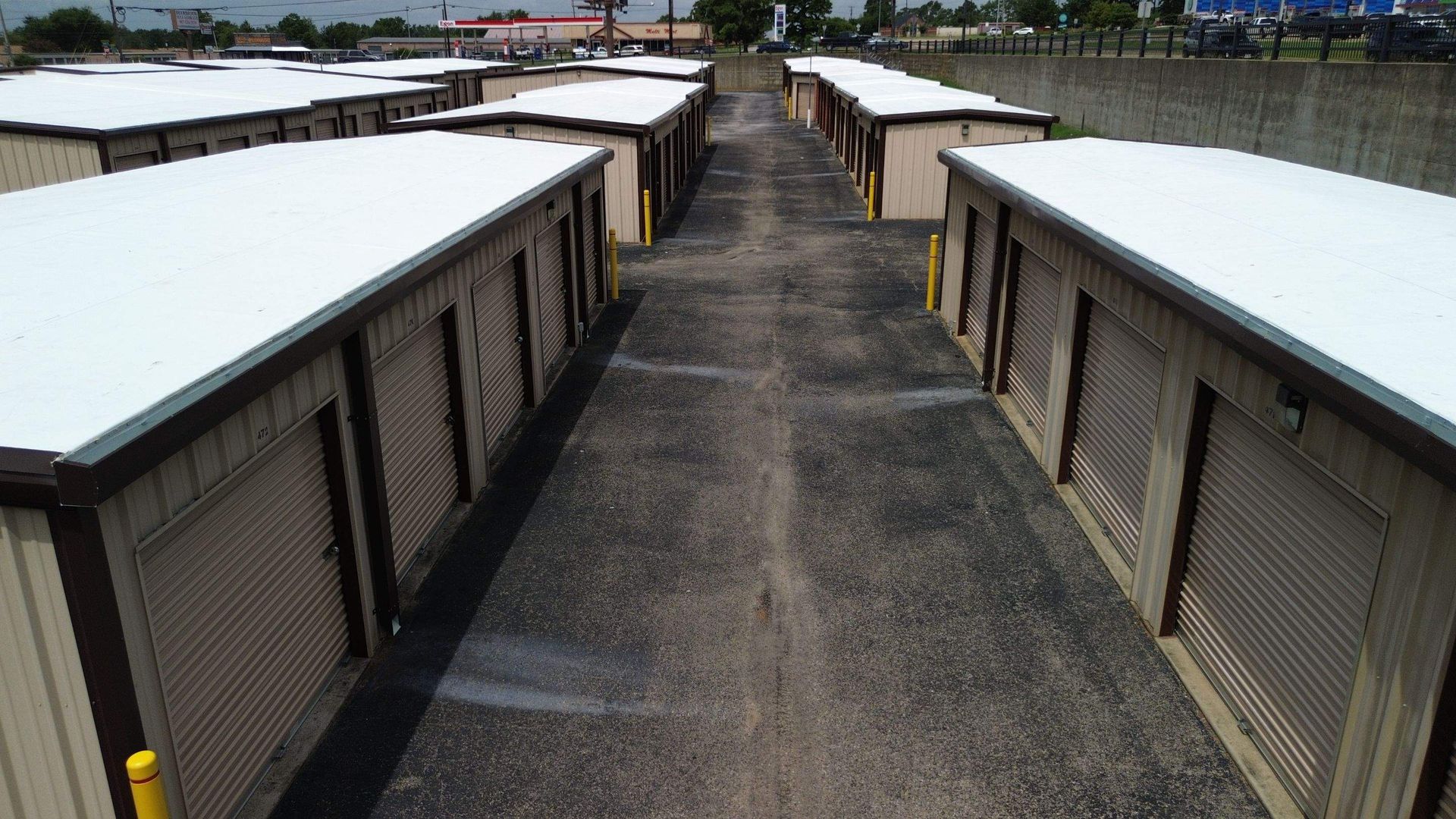 A row of storage units with white roofs are lined up in a parking lot.