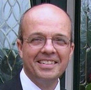 A bald man wearing glasses and a suit is smiling.