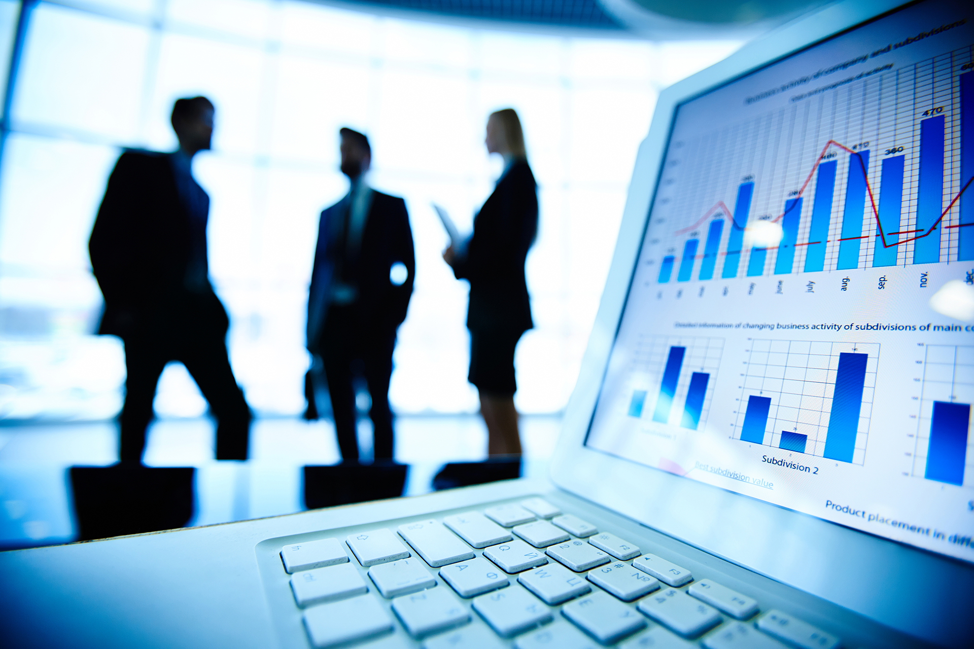 Laptop displaying business data, three blurred figures in the background.