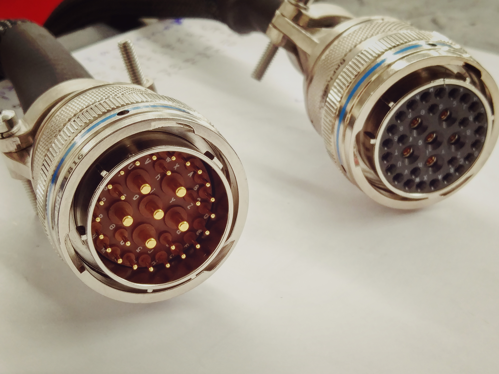 Two circular electrical connectors with multiple pins, silver metal casing, on white paper.