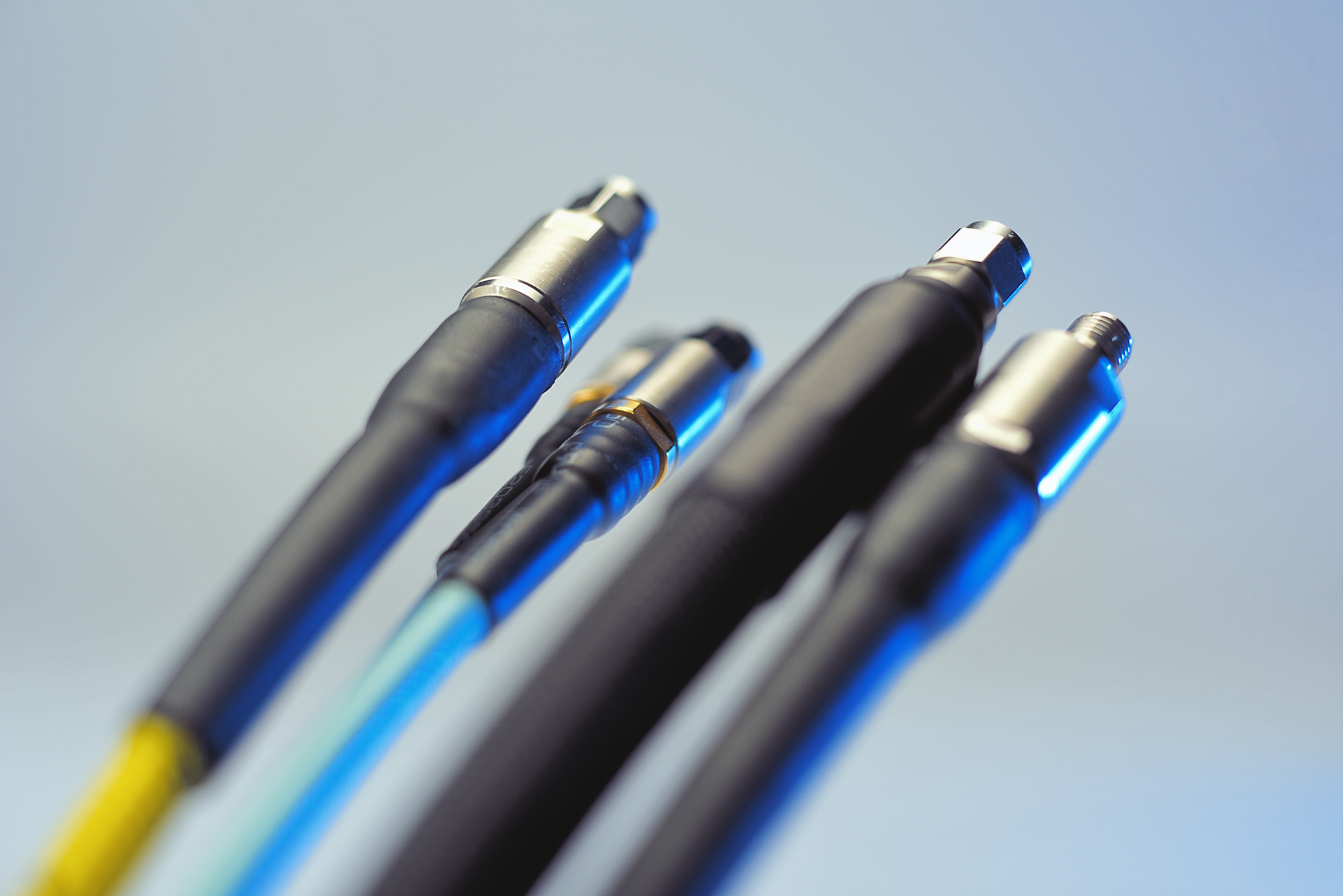 Close-up of four fiber optic cables with metal connectors and varying colored insulation.
