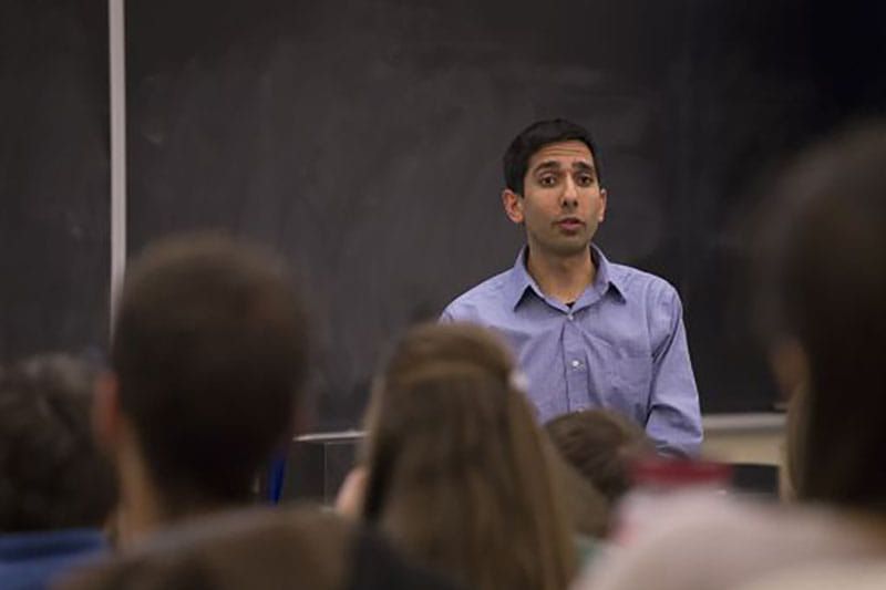 A man is giving a lecture to a group of students in front of a blackboard.