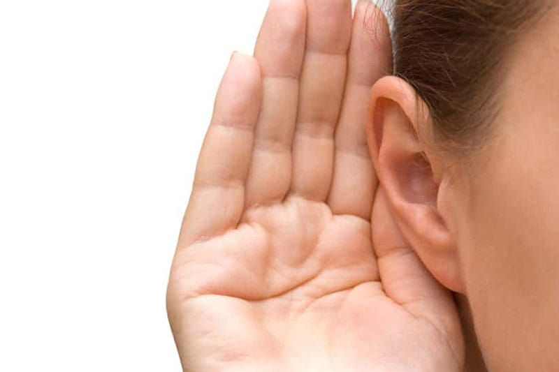 A woman is holding her hand to her ear to hear something.