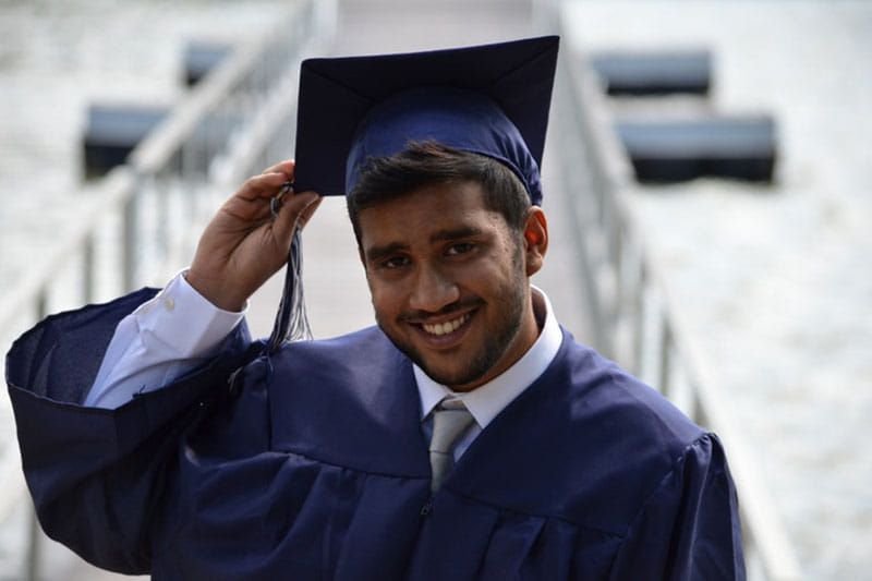 A man in a graduation cap and gown is smiling.