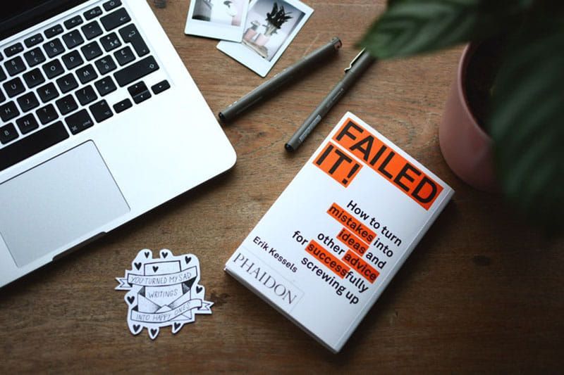 A book titled failed it is sitting on a wooden table next to a laptop.