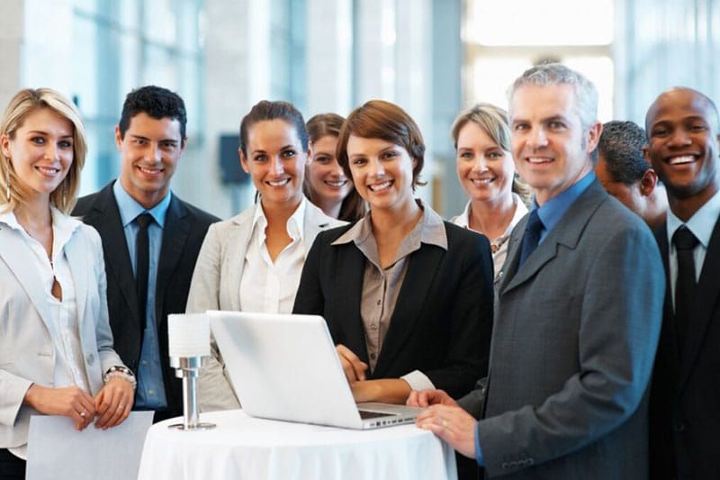 A group of business people standing around a table with a laptop on it.