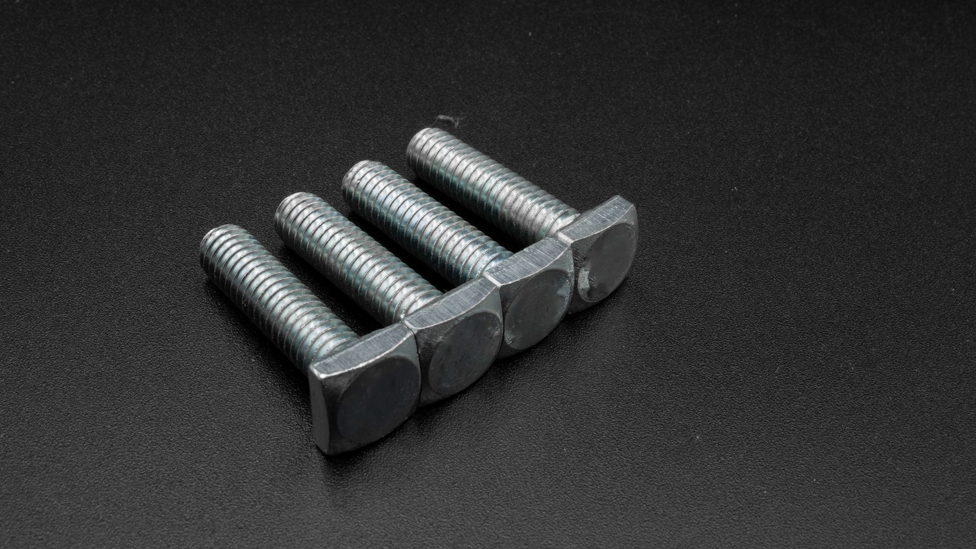 Four square screws are stacked on top of each other on a black surface.