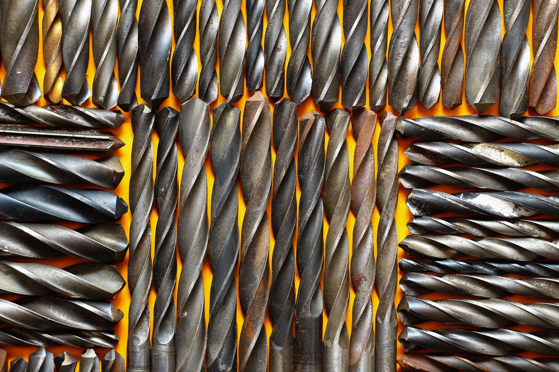A bunch of drill bits are lined up on a yellow surface