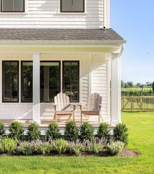 A white house with a porch and chairs in front of it.