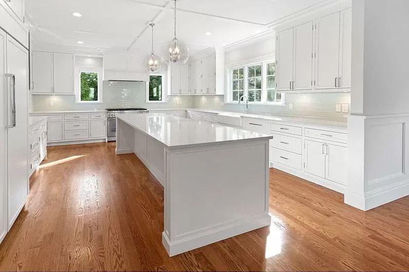 A large kitchen with white cabinets and hardwood floors.