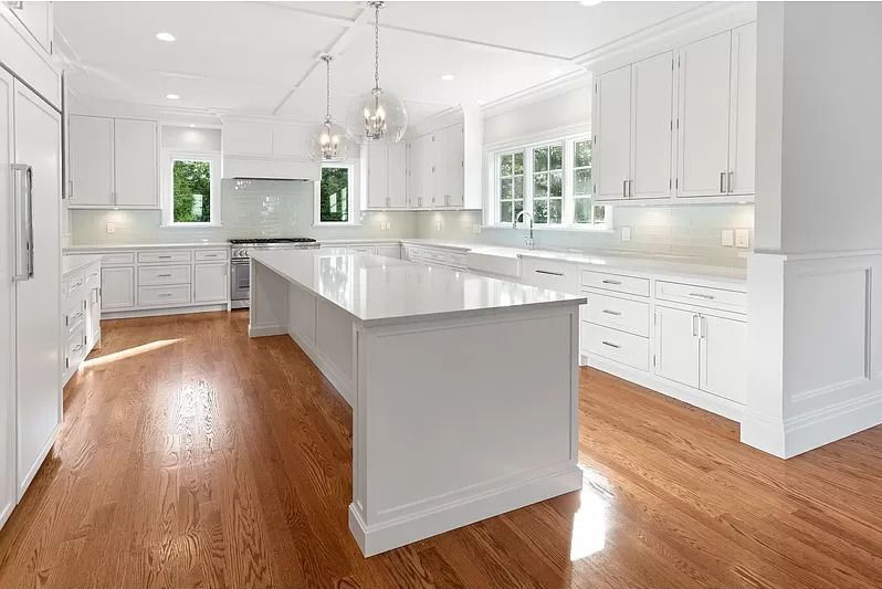 A kitchen with white cabinets and hardwood floors and a large island.