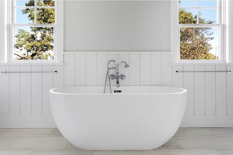 A white bathtub in a bathroom next to a window.