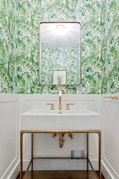 A bathroom with a sink , mirror , and green wallpaper.