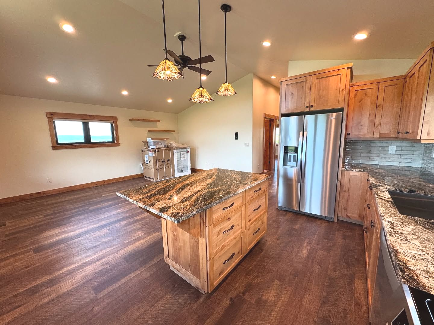 Spacious kitchen with wood cabinets, granite countertops, island, stainless steel fridge, hardwood floors.