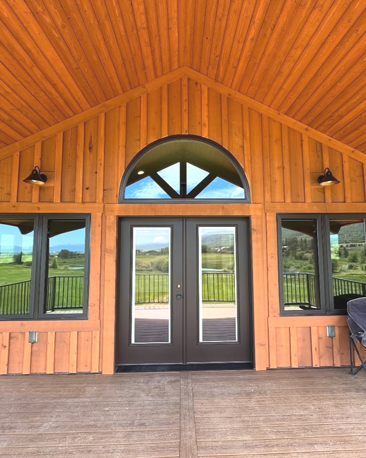 Wooden lodge exterior with double doors, arched window, side windows, and sconces.