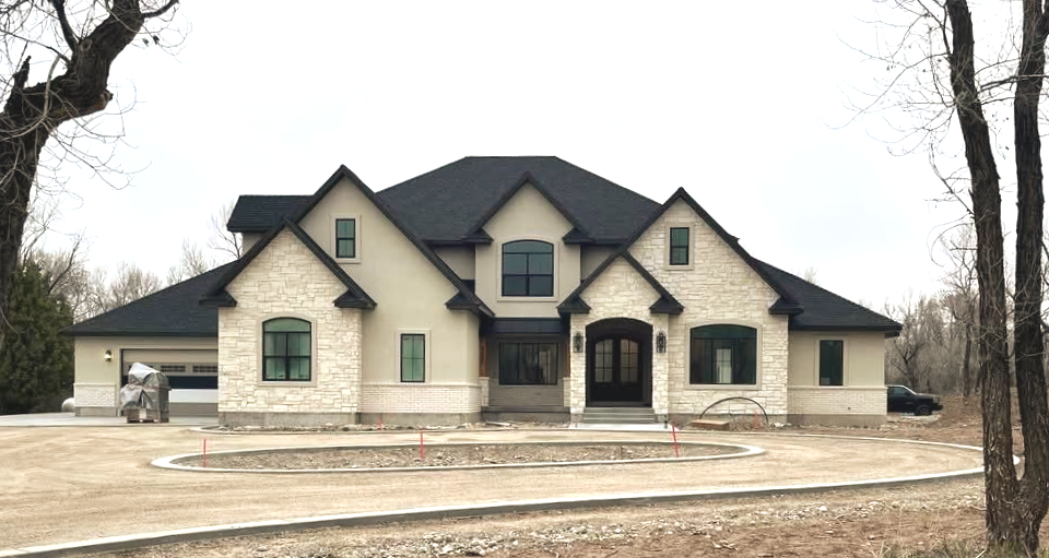 A large, light-colored stone house with a black roof under a cloudy sky.