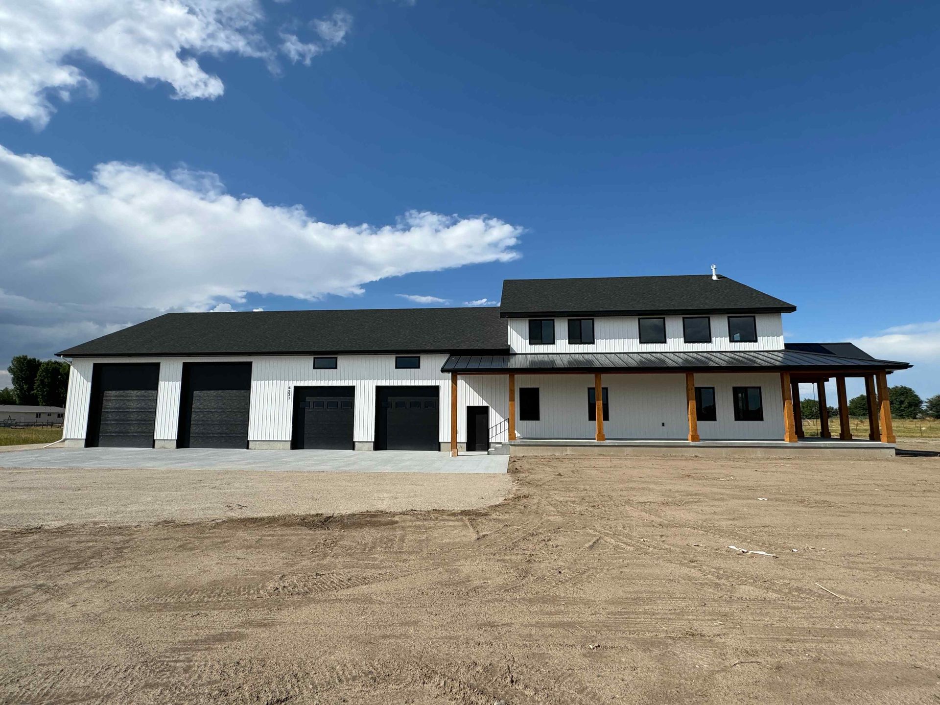 White two-story house with large windows and a brick chimney on a gravelly hill under a blue sky.