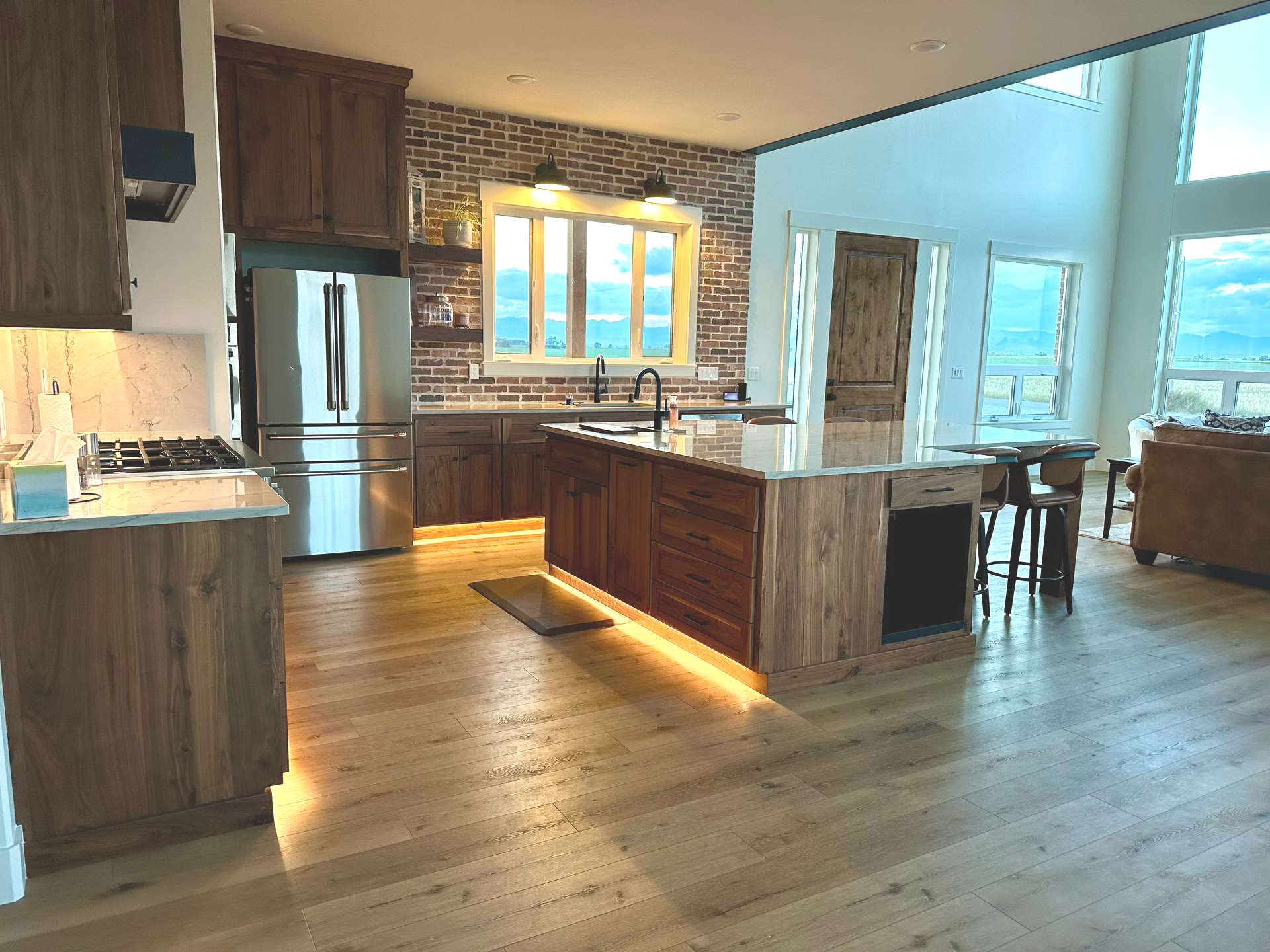 Modern kitchen with wood cabinets, island, and brick backsplash; natural light floods the space.