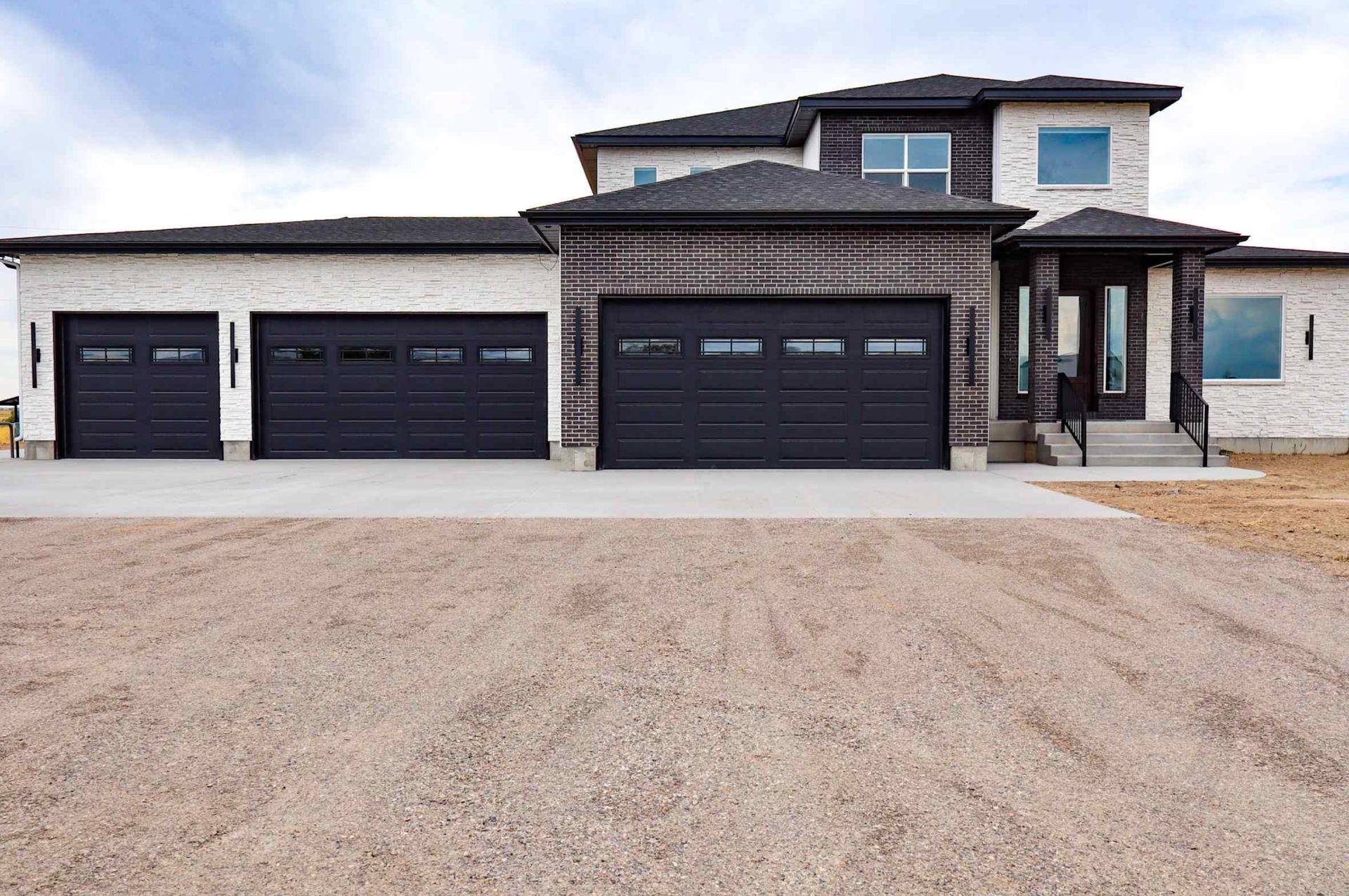White two-story house with large windows and a brick chimney on a gravelly hill under a blue sky.