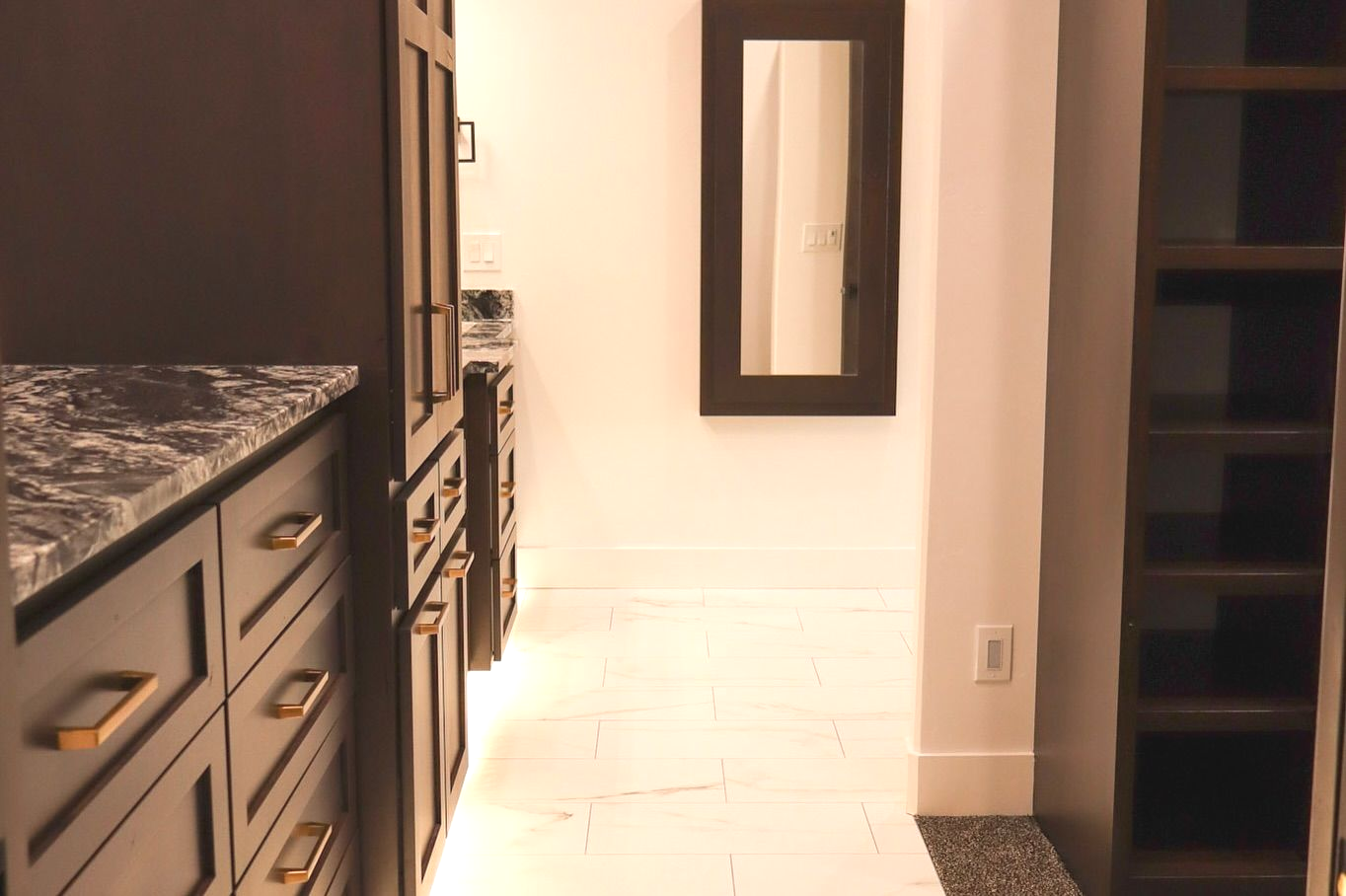 Bathroom with dark cabinetry, marble countertop, white tile floor, mirror, and open shelving.