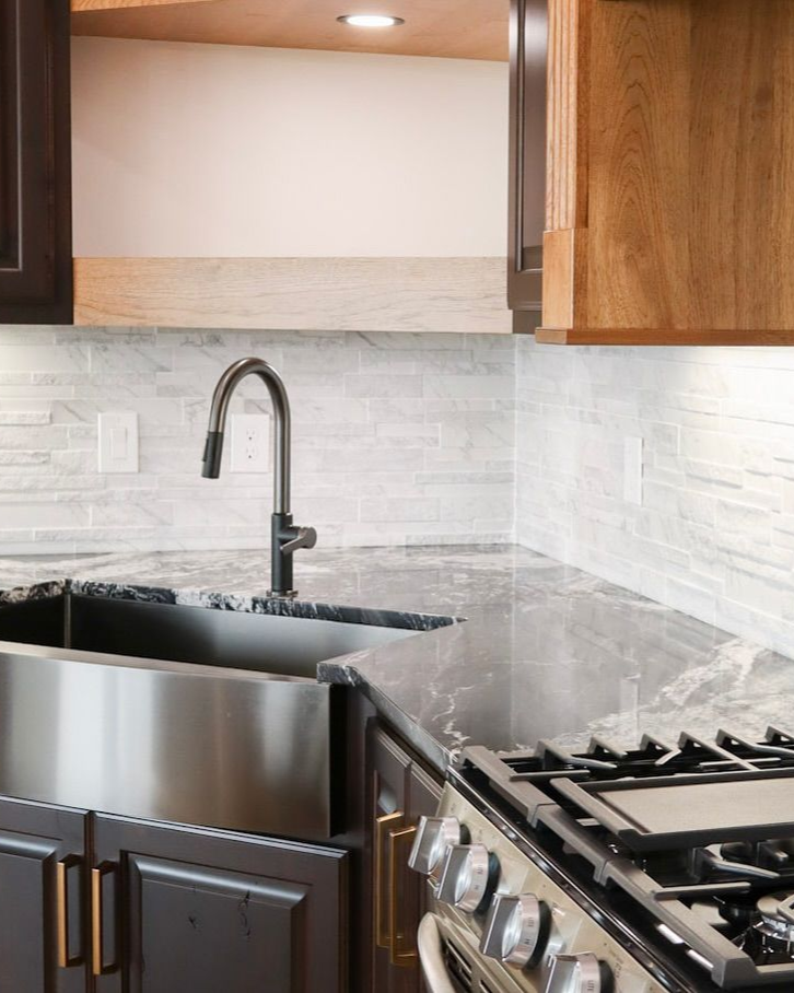 Stainless steel kitchen sink and faucet with dark cabinets, a grey countertop, and stove.