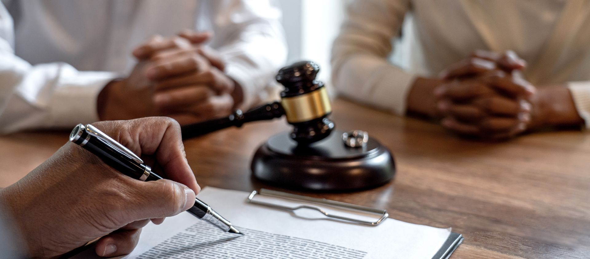 Gavel on a desk next to a balance scale and legal documents; a hand in background.