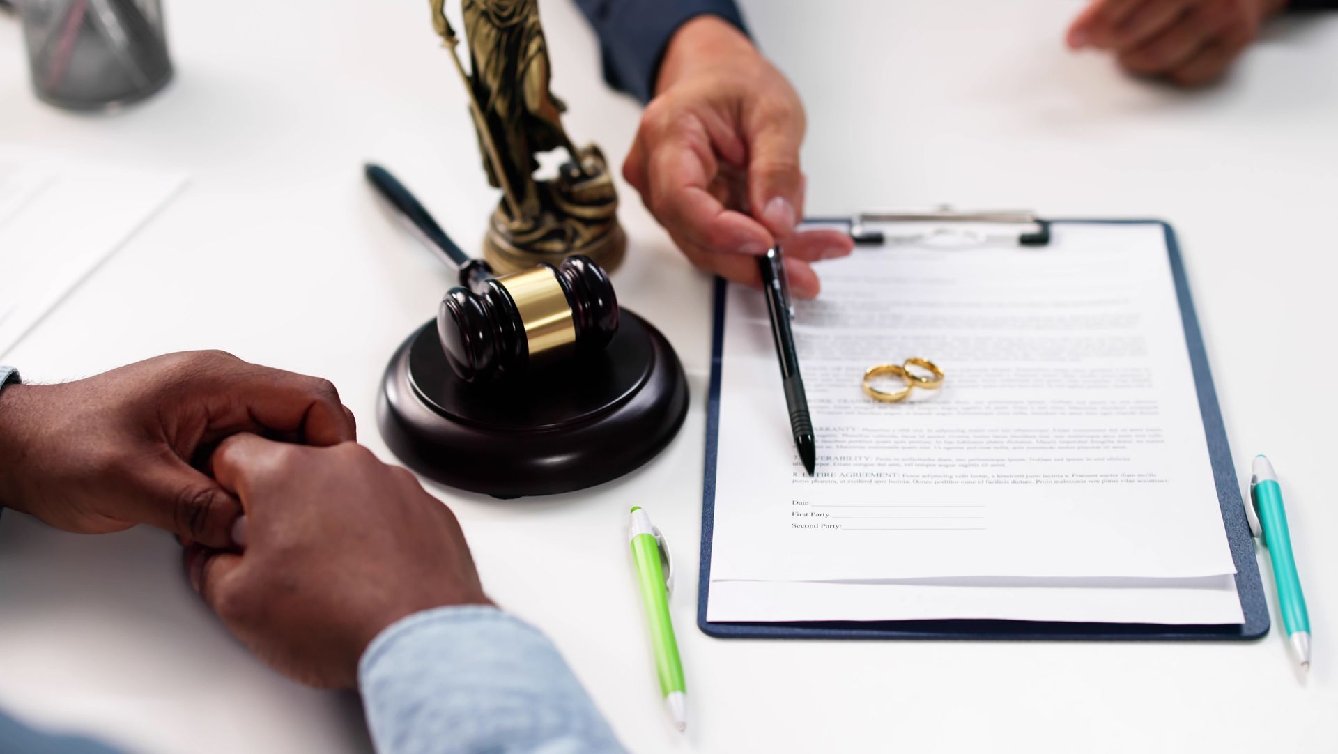 Hands pointing at divorce papers with wedding rings and a gavel.