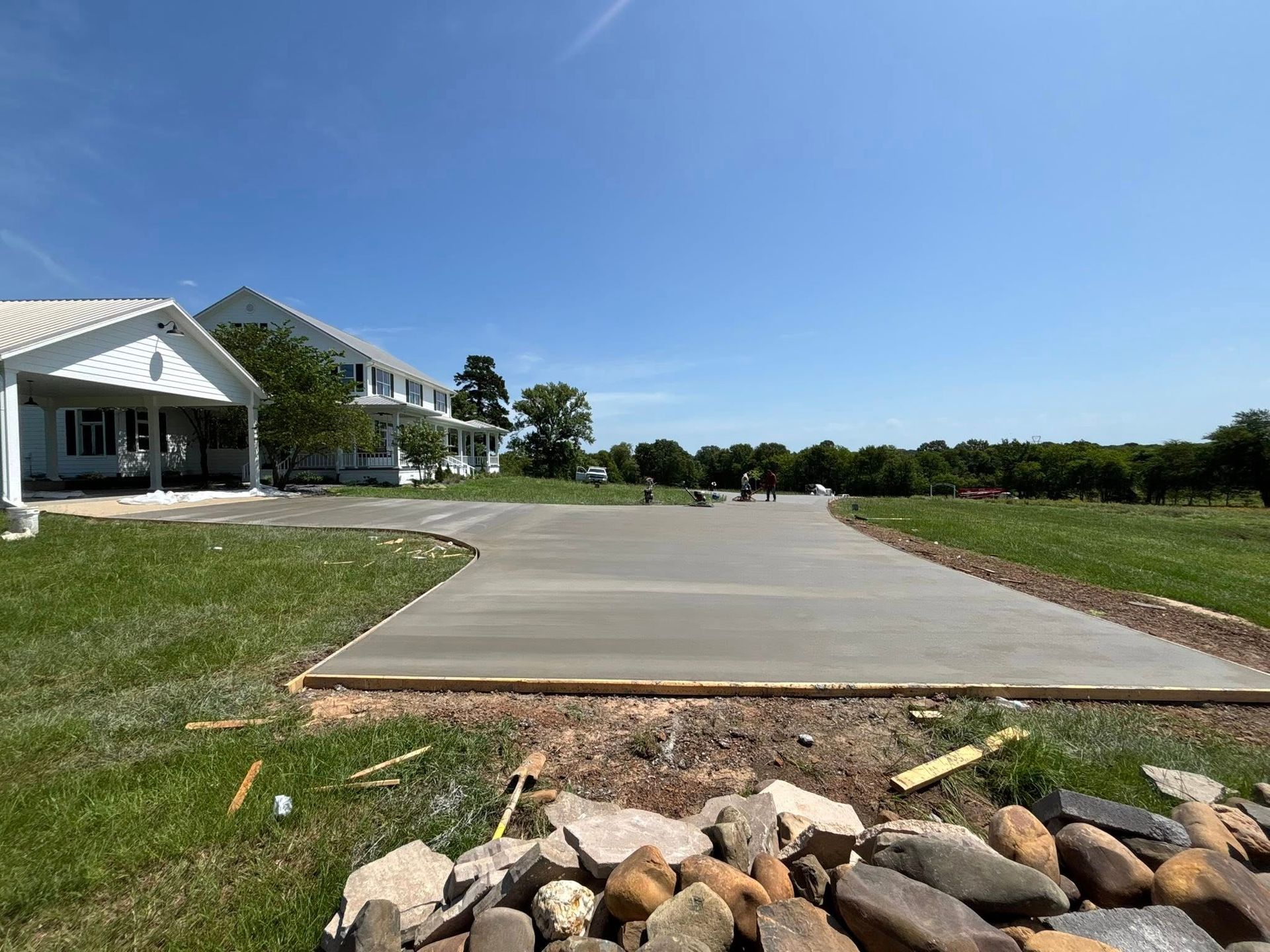 Newly poured concrete driveway leading to a white building under a blue sky, surrounded by green grass.