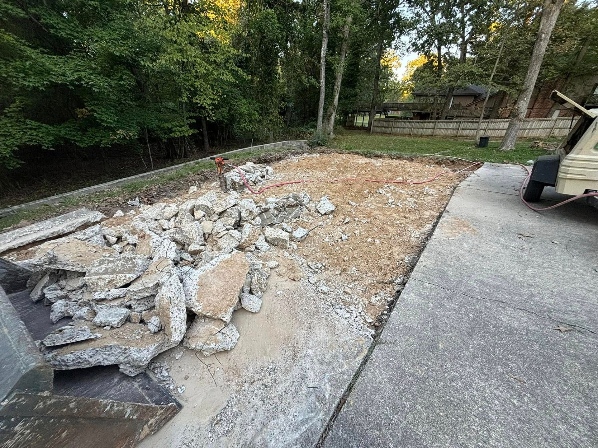 Concrete demolition area next to a driveway. Concrete rubble on a dirt surface surrounded by trees.