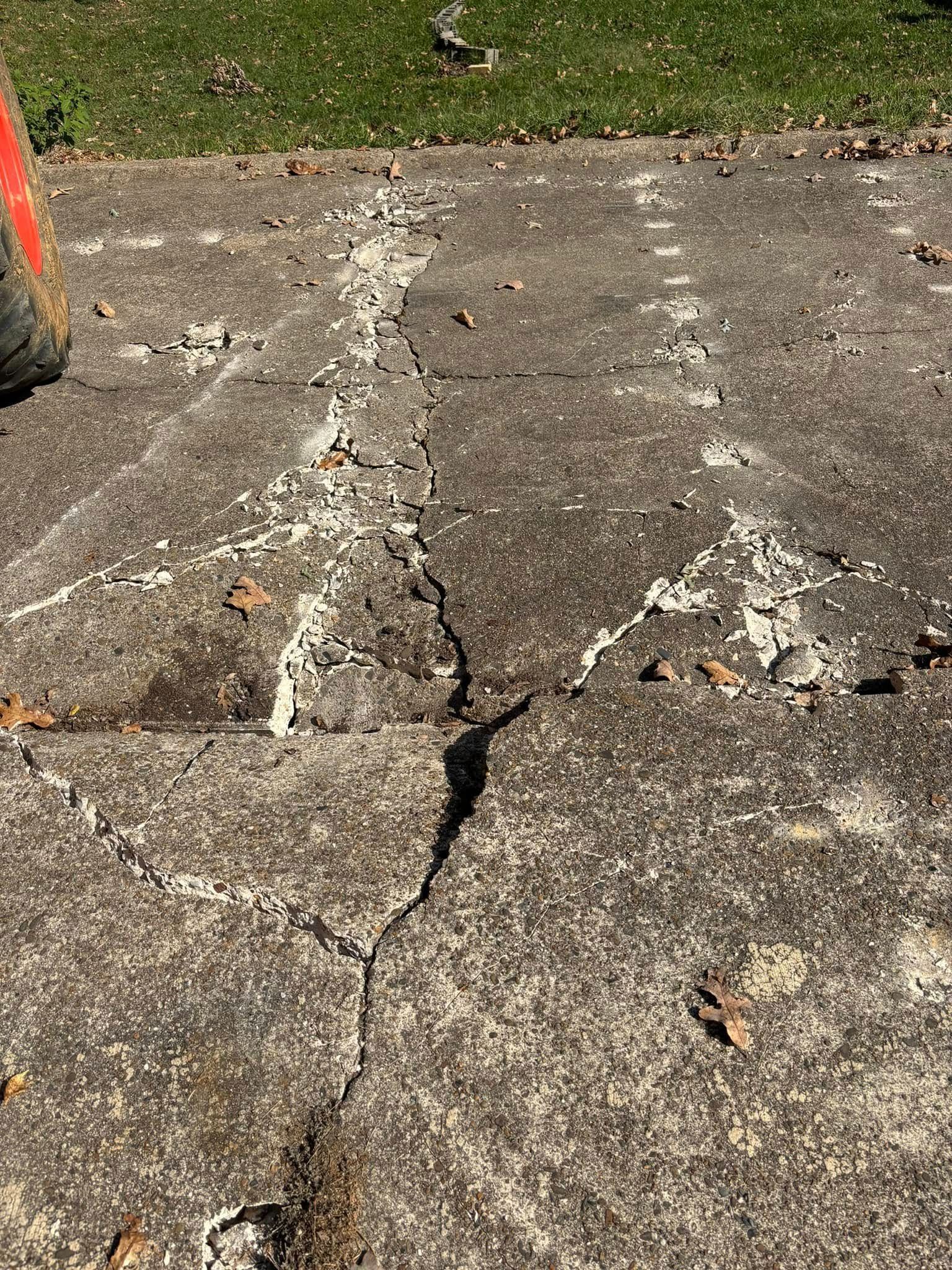 Damaged concrete walkway with cracks, debris, and white patching in a park setting.