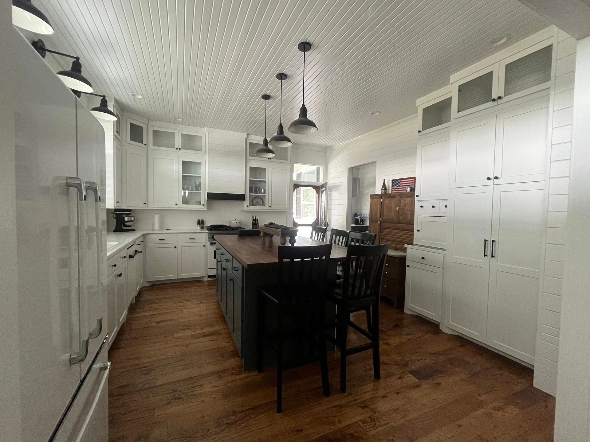 White kitchen with wood floors, island, pendant lights, and stainless steel appliances.