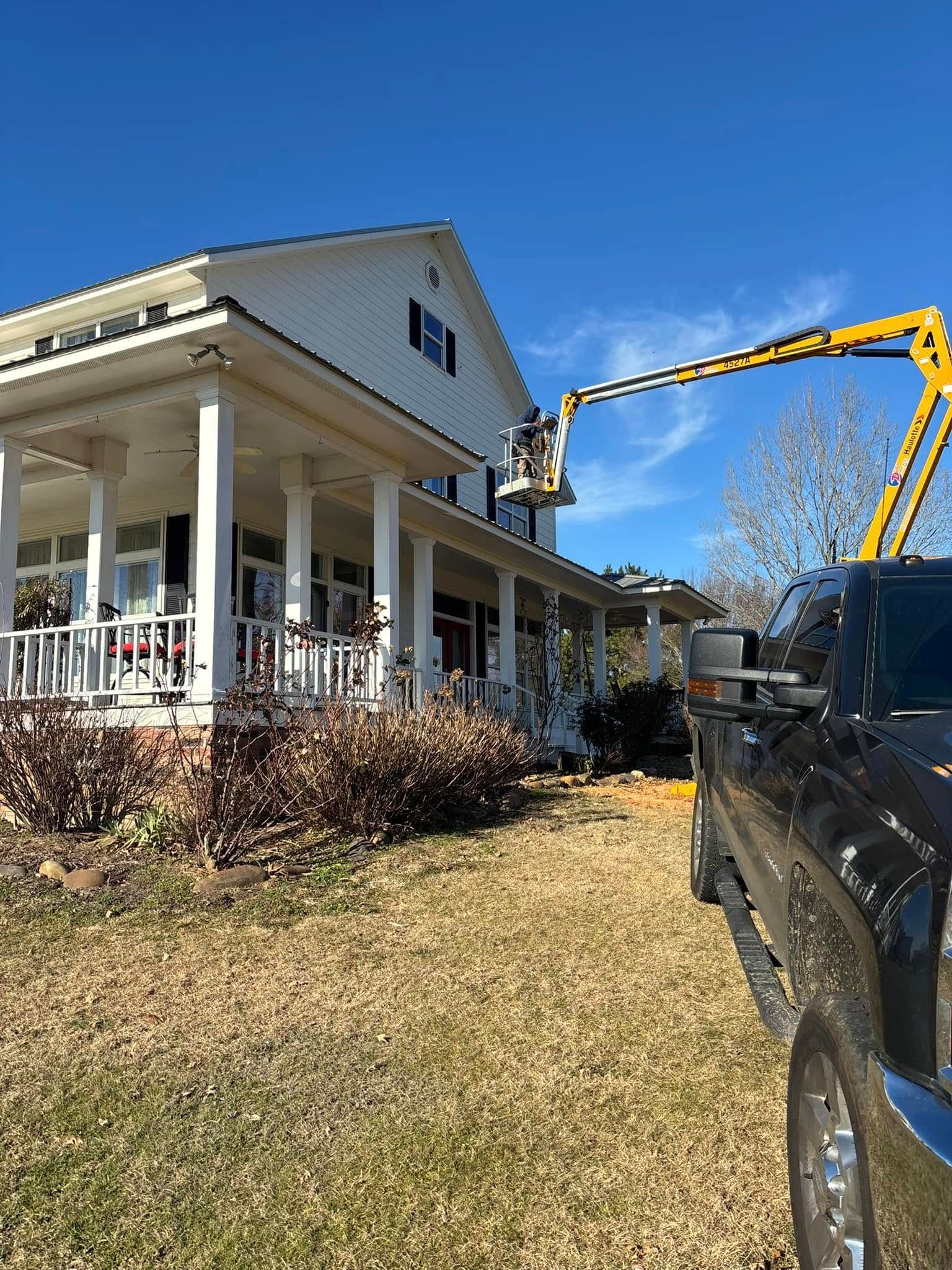 A yellow lift truck working on the roof of a two-story white house with a porch.