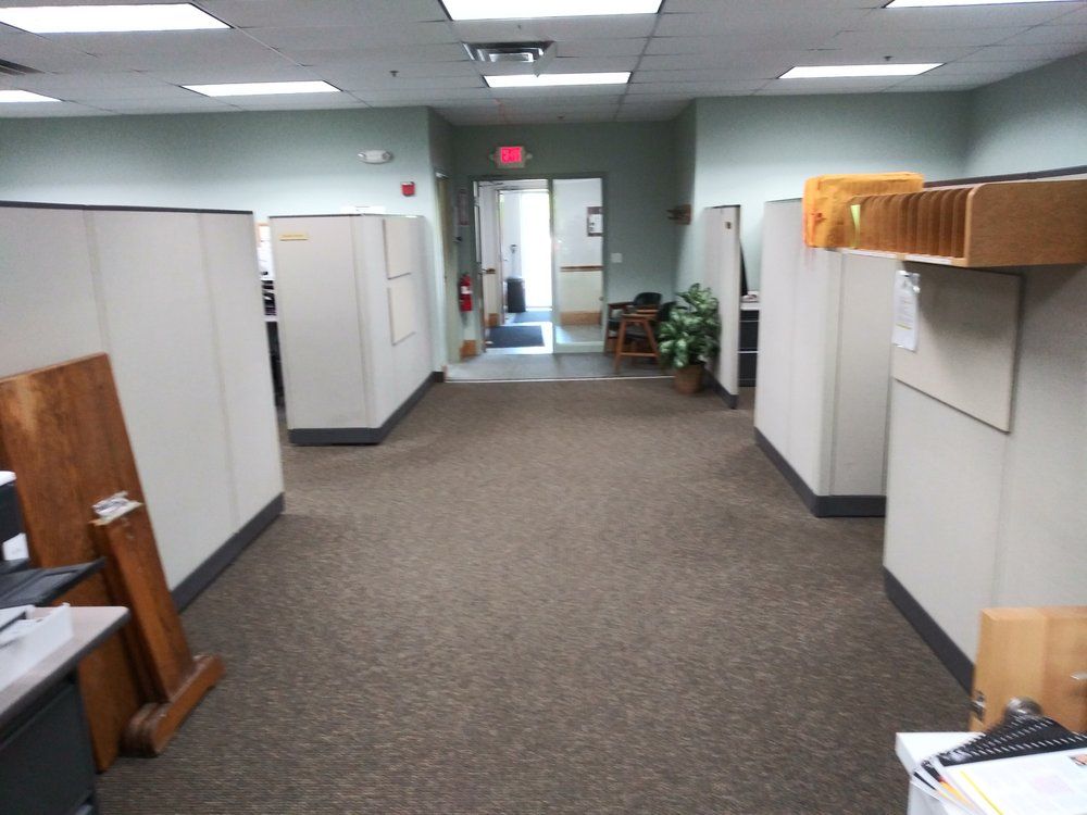 A hallway with cubicles and a red exit sign