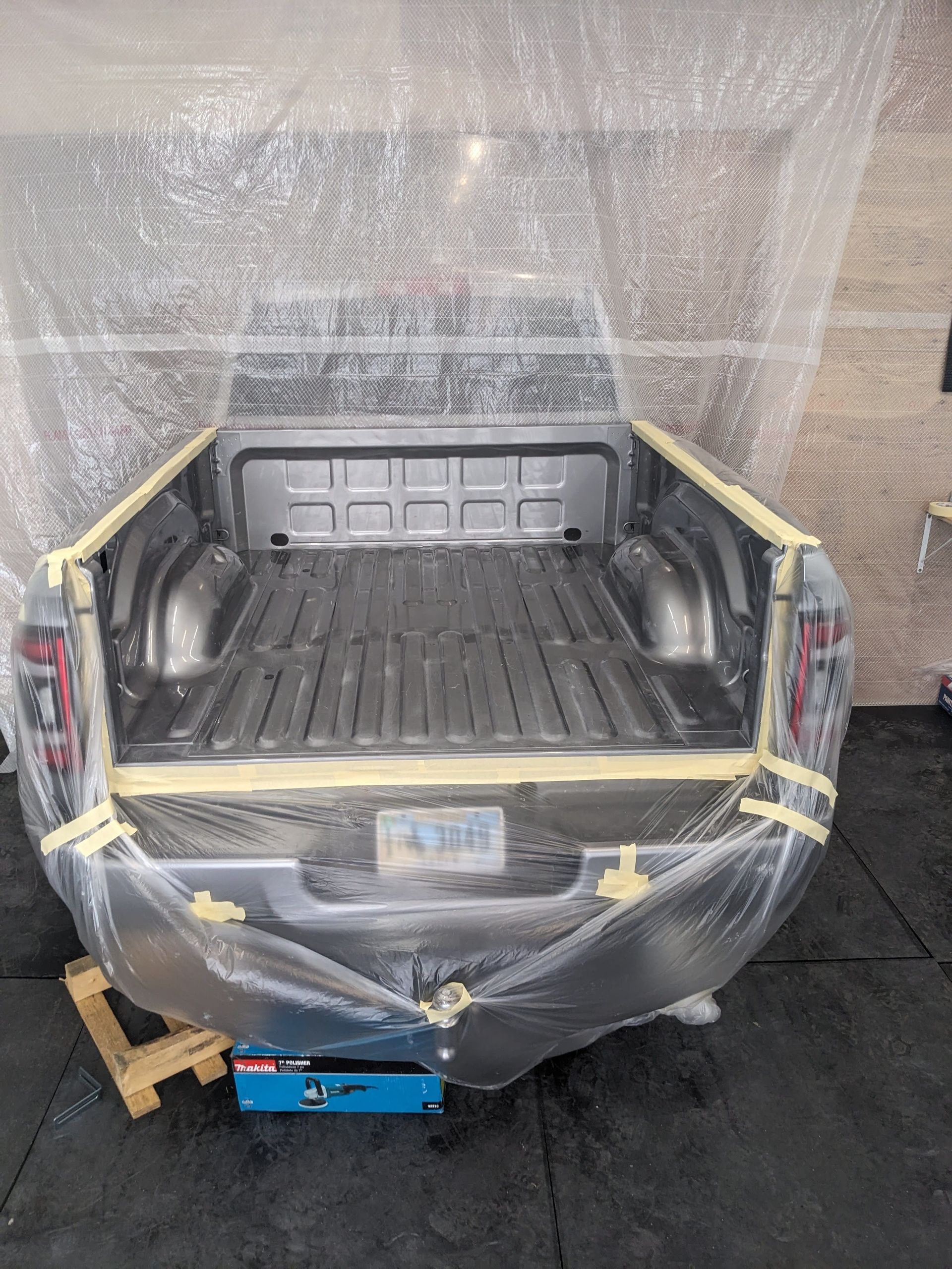 A truck bed, taped and covered in plastic, ready for painting inside a workshop.