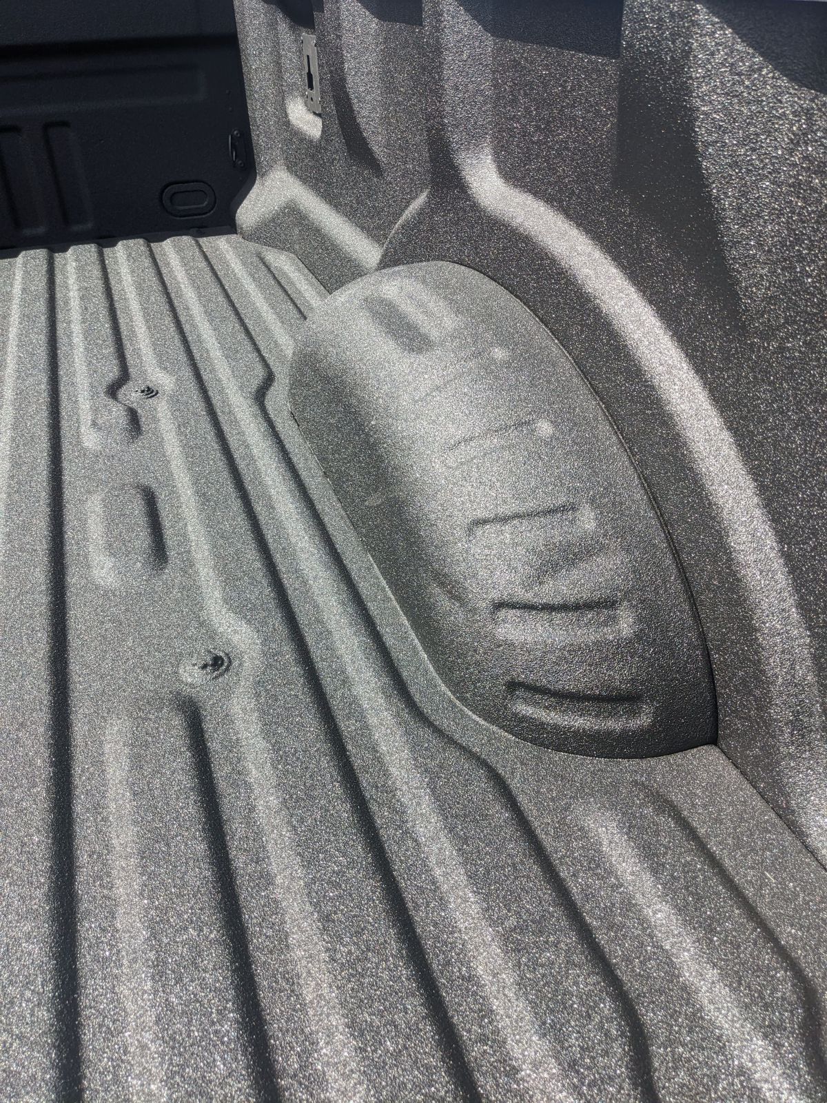 Truck bed with textured black liner, wheel well visible.