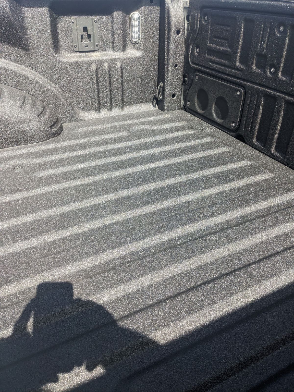 Textured, black truck bed with ridged floor, power outlets on the wall.