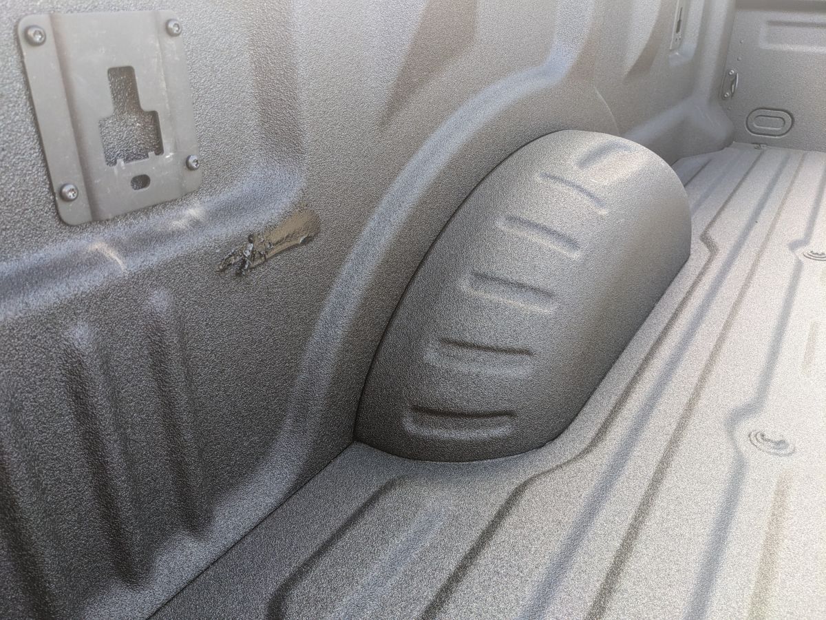 Textured bed liner inside of a gray truck bed, featuring a wheel well and tie-down locations.