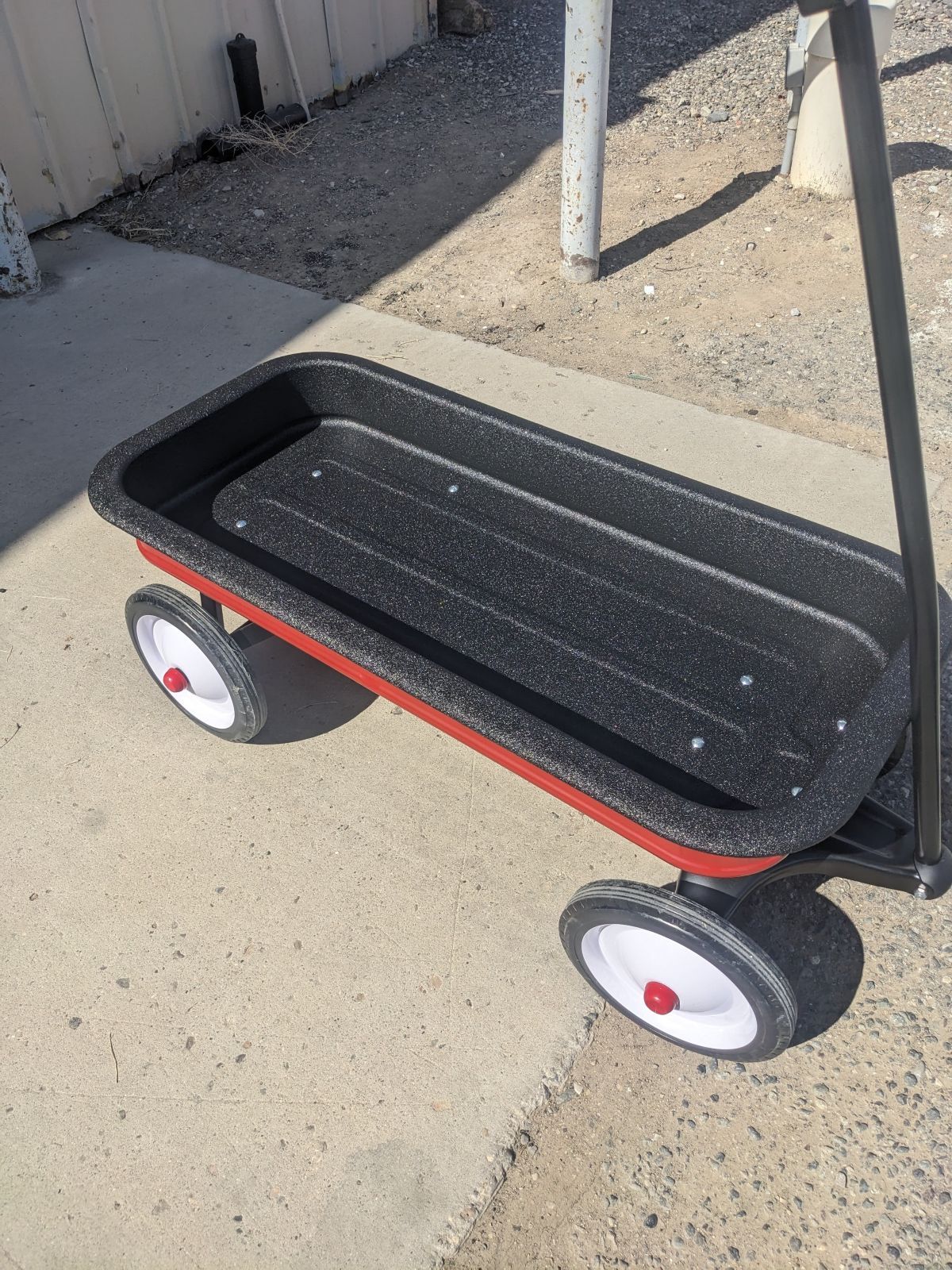 Red and black wagon with white wheels on a concrete surface.