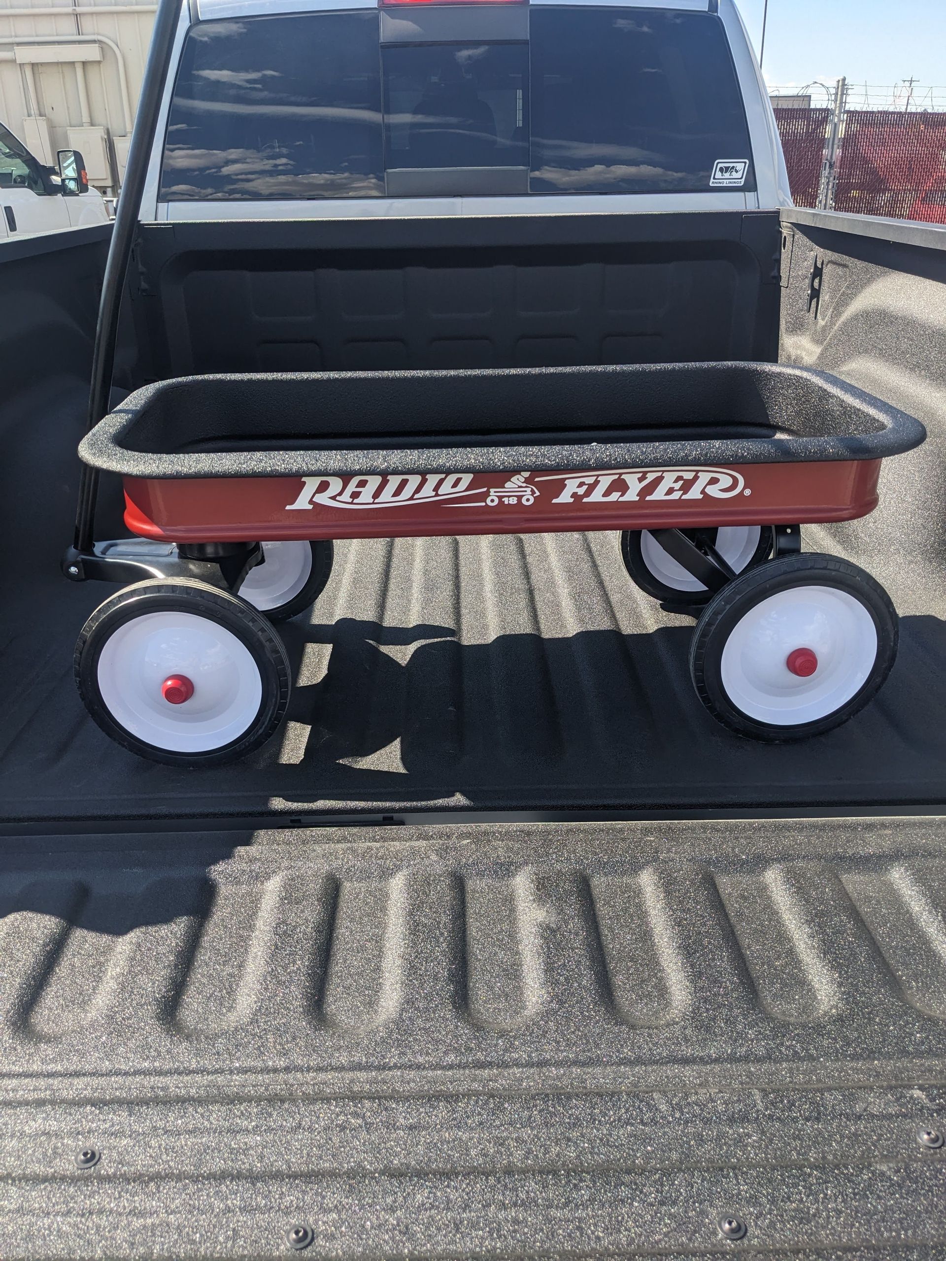 Red Radio Flyer wagon in the bed of a black pickup truck.