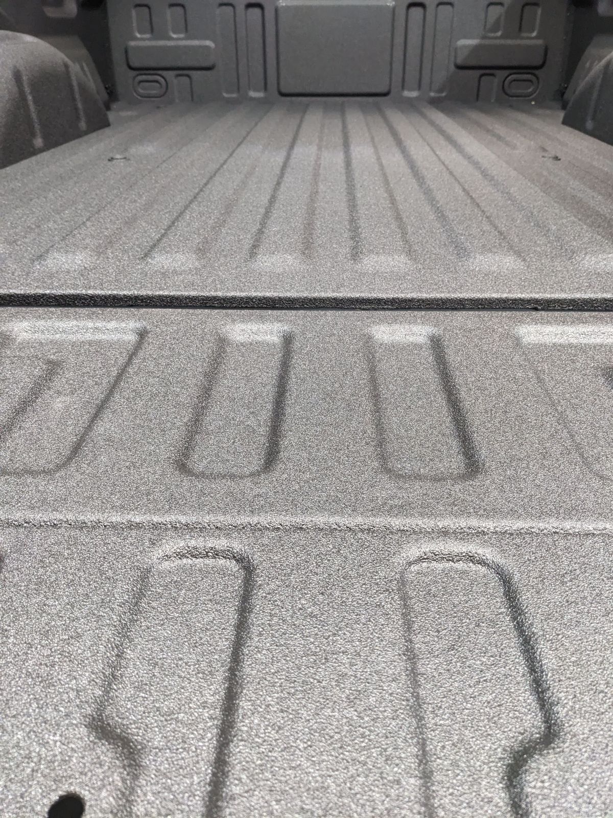 Textured black bedliner in a truck bed, featuring molded grooves and a grainy surface.