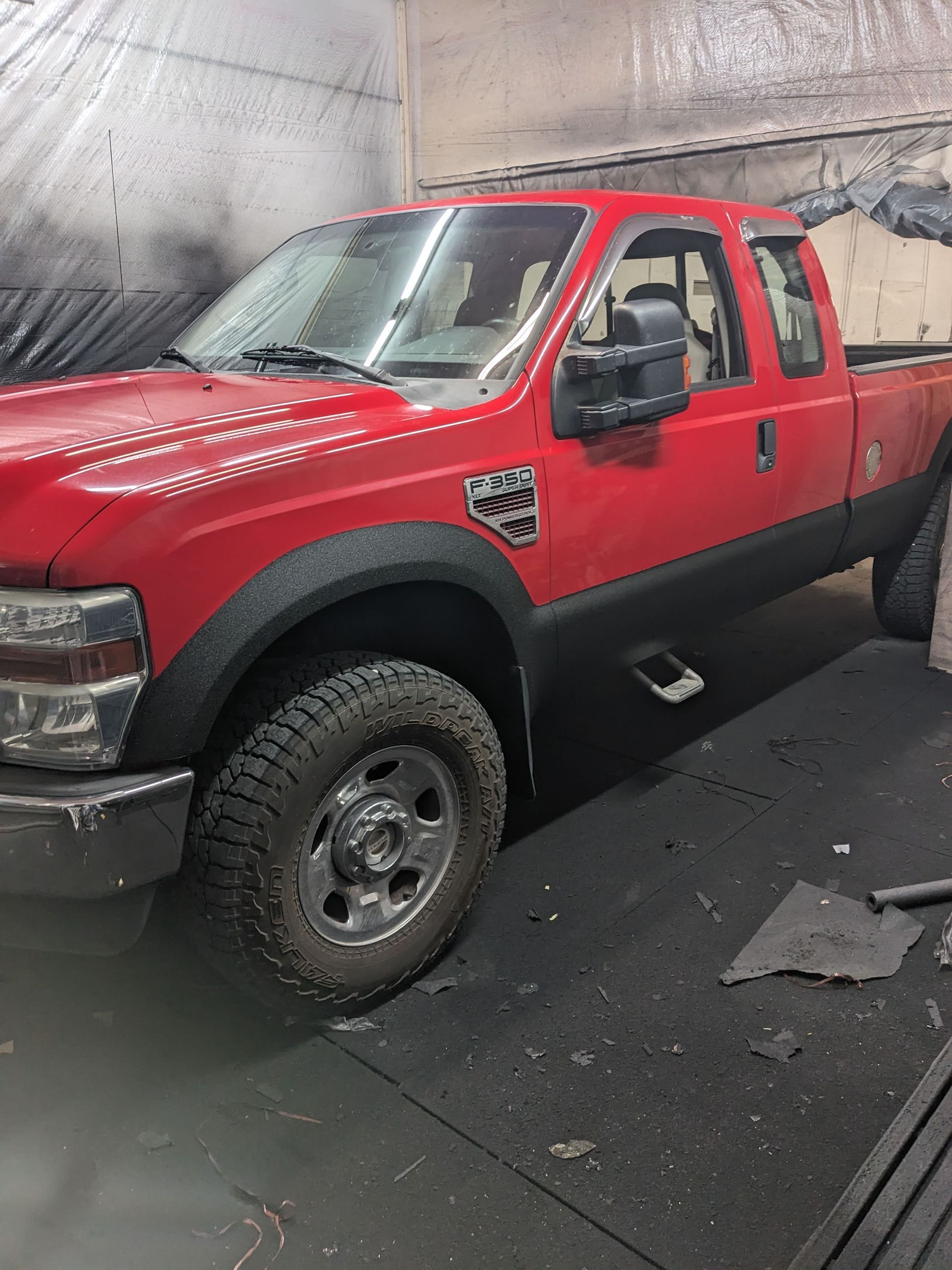 Red Ford pickup truck, black fenders, inside a garage with dark surfaces.