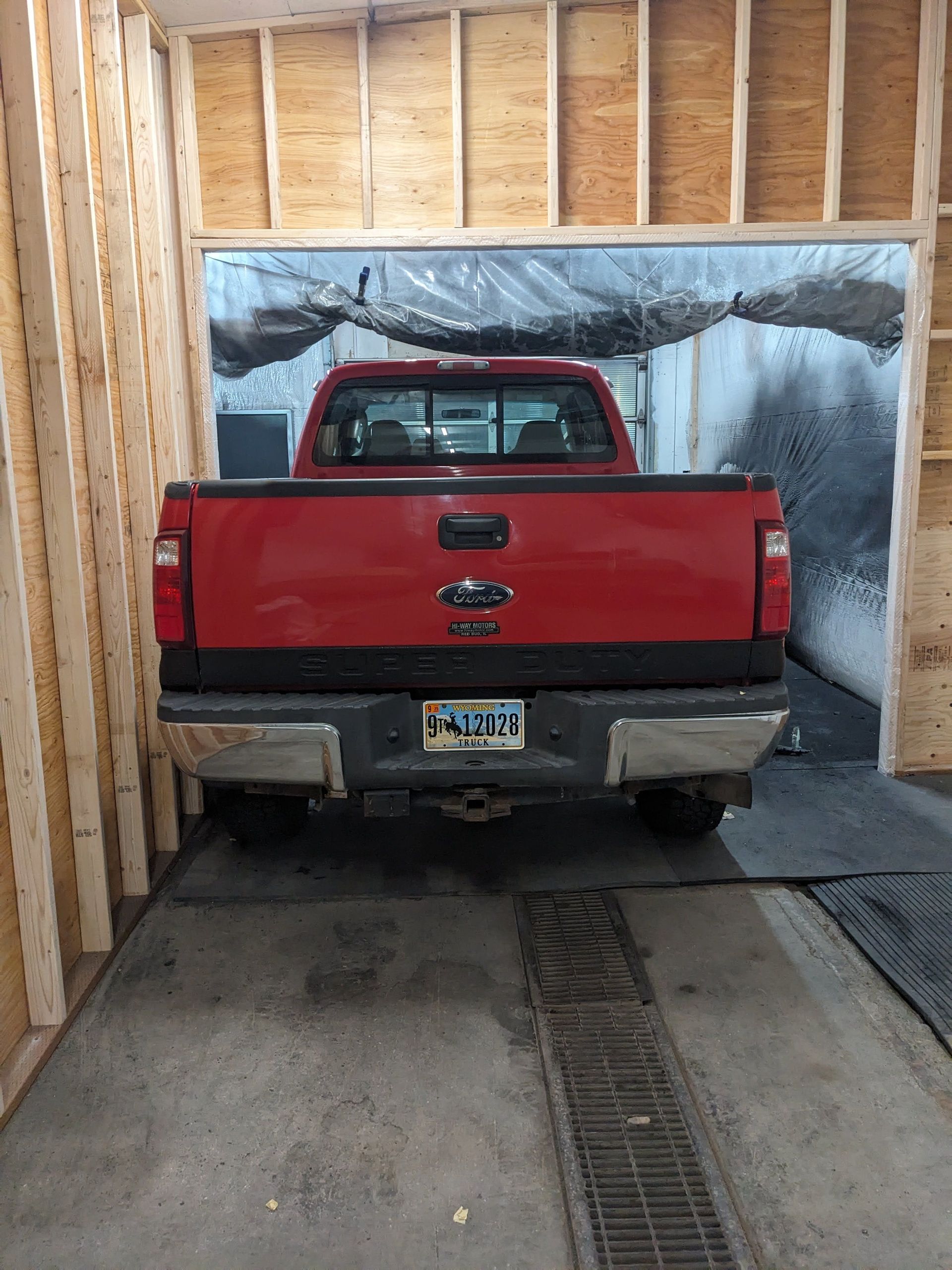 Red pickup truck parked inside a wooden structure. Rear view with a license plate and dark bumper.