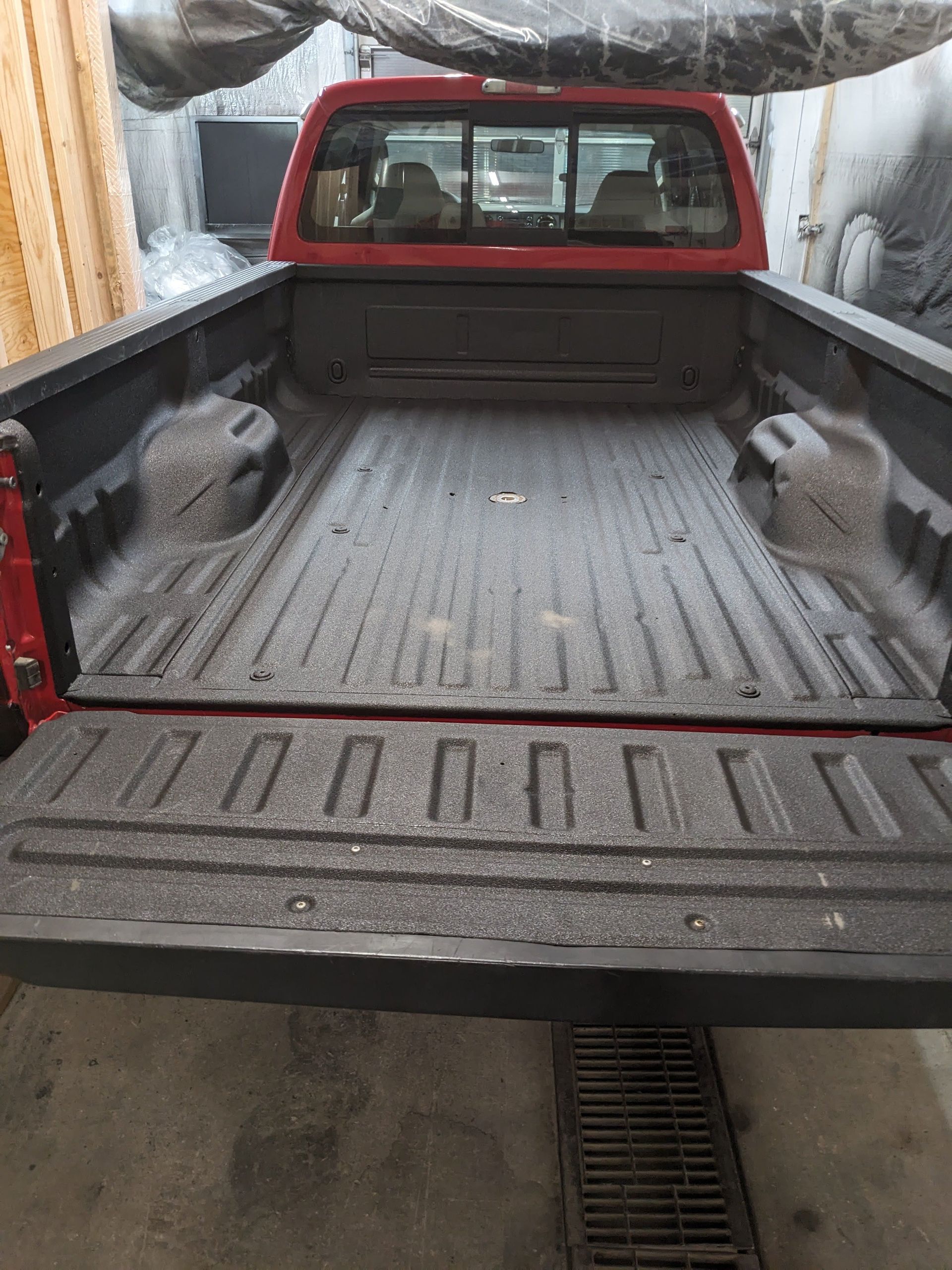 Red pickup truck bed with bedliner, black tailgate, and rear cab.