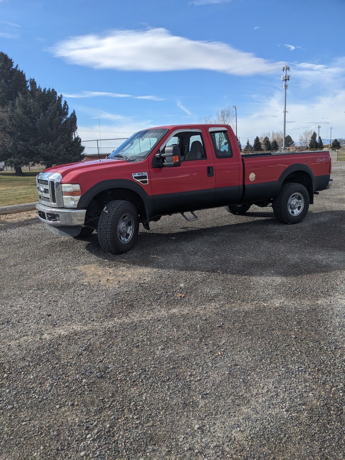 Red Ford pickup truck parked on gravel under a blue sky.