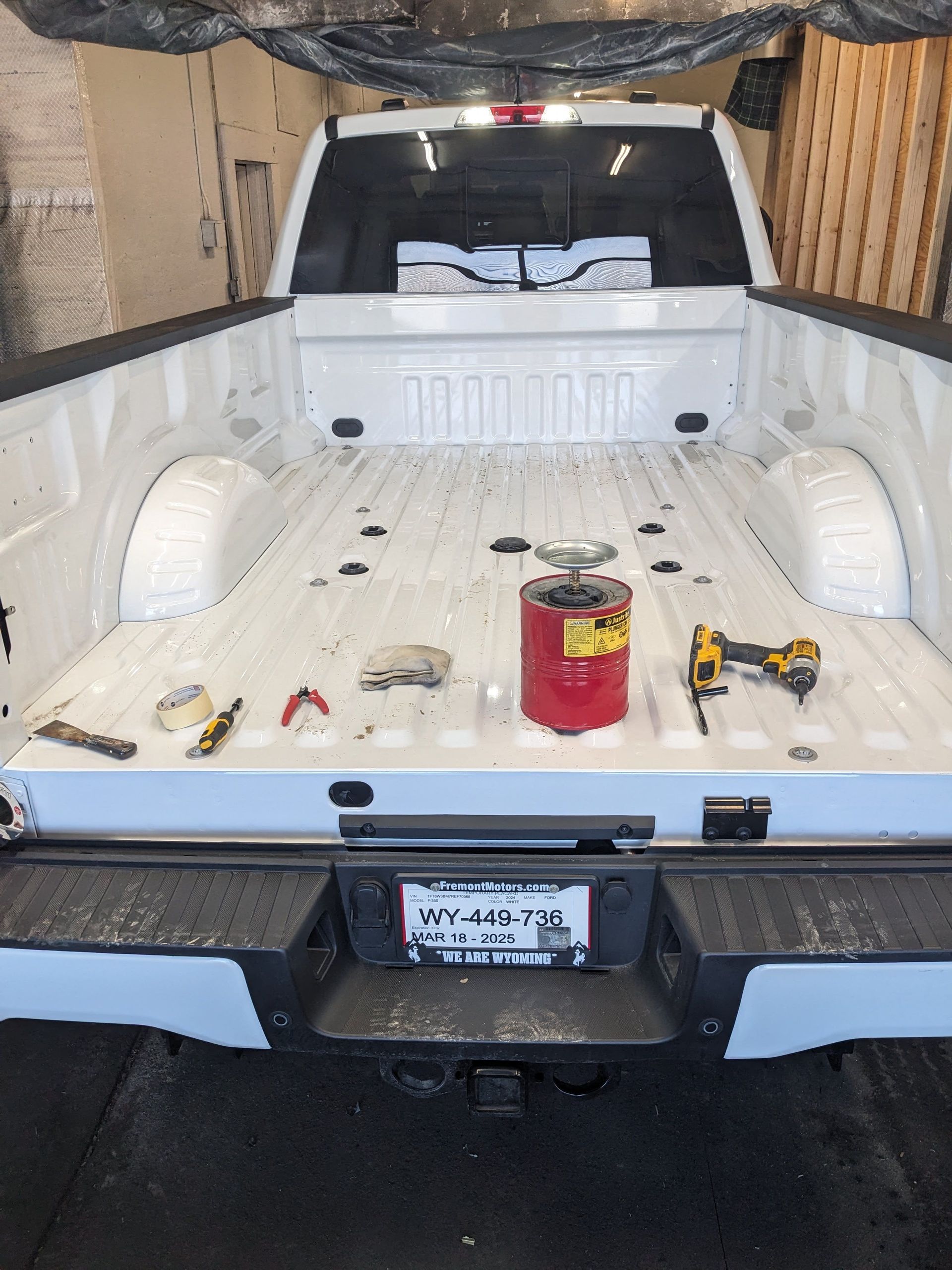 White truck bed with tools and a red propane tank.