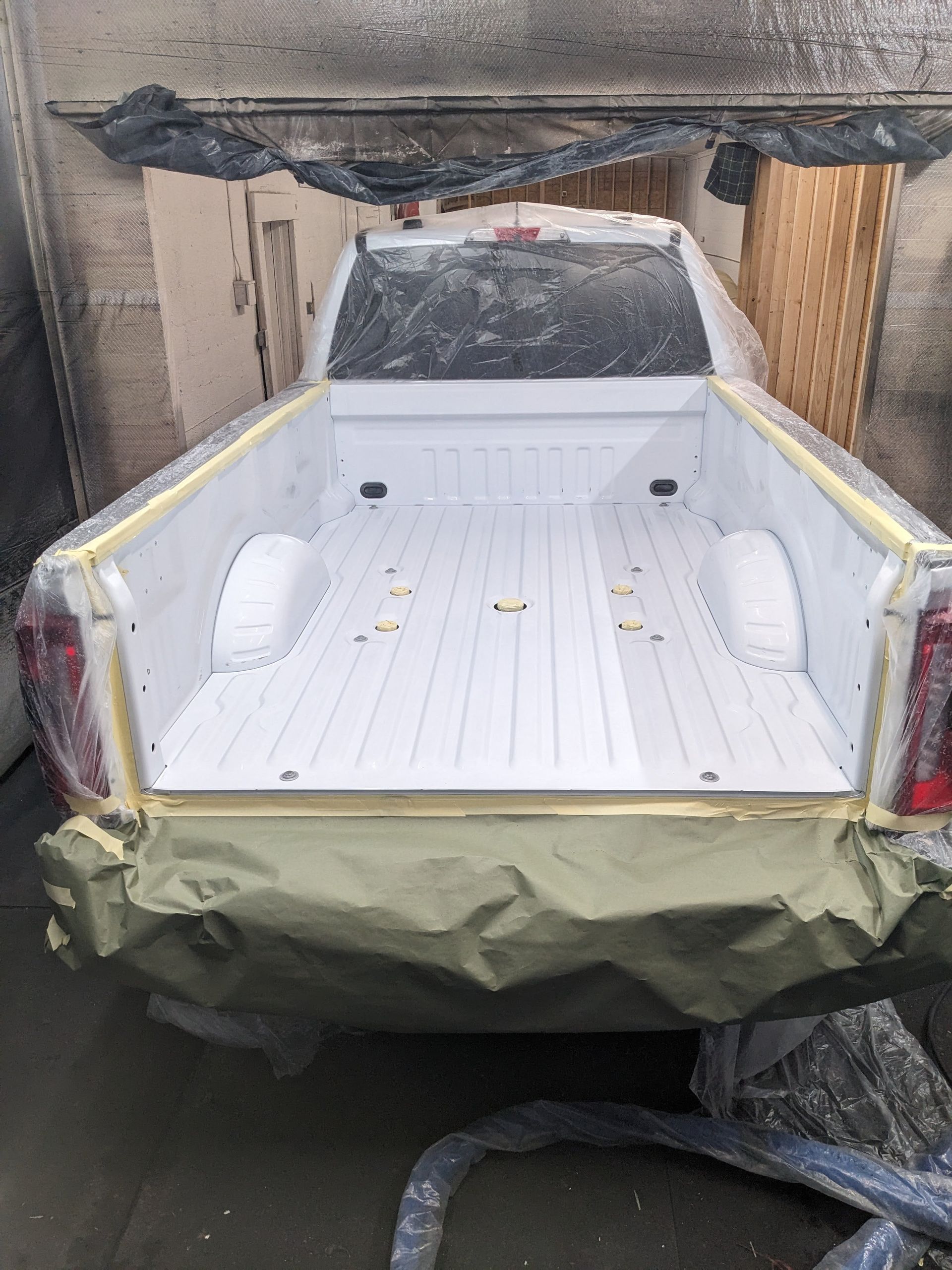 White pickup truck bed masked and painted, in a paint booth.