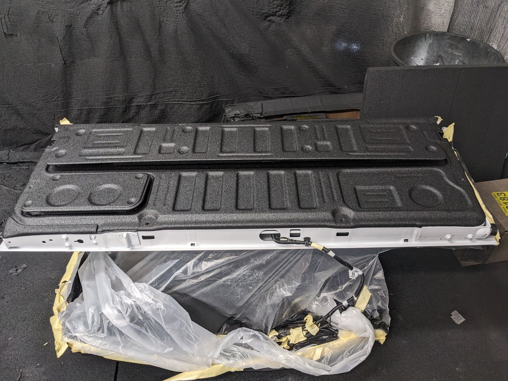 Truck tailgate with bedliner coating, resting on plastic sheet, indoors.